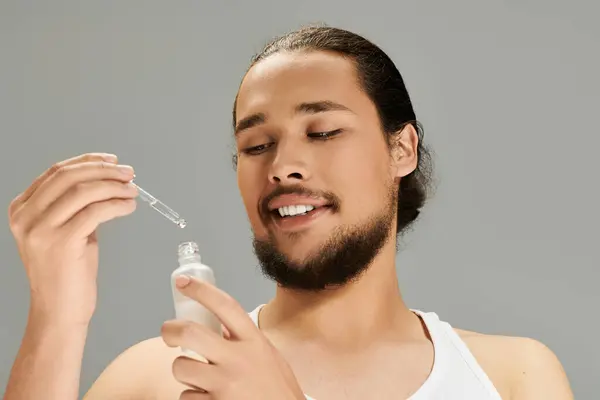 Young bearded man carefully uses a dropper to apply a serum while smiling joyfully. — Stock Photo