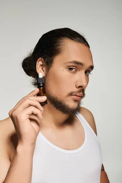 A young man with a beard showcases a small bottle while posing against a soft backdrop. — Stock Photo