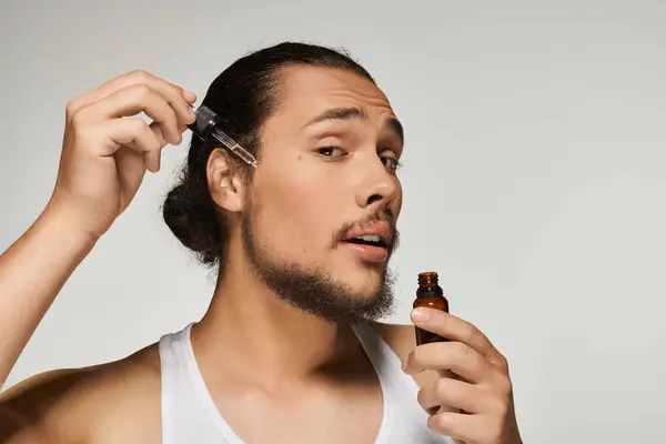 A young bearded man focuses on enhancing his grooming routine, applying oil to his beard. — Stock Photo