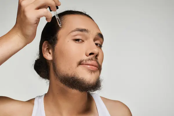 A handsome young man enhances his beard with a dropper, showcasing his grooming routine. — Stock Photo