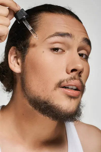 Young man with a beard focuses on applying a skincare serum to his handsome face. — Stock Photo