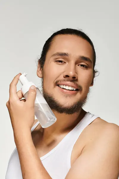 A charming young man joyfully applies skincare, showcasing his healthy beard in a well lit studio. — Stock Photo