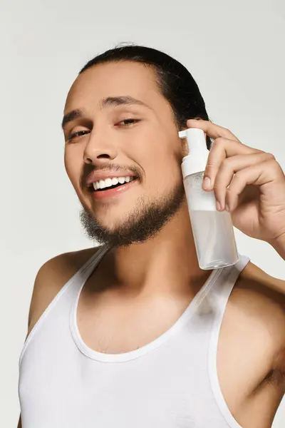 A youthful man smiles confidently while using a skincare spray, focusing on self grooming. — Stock Photo