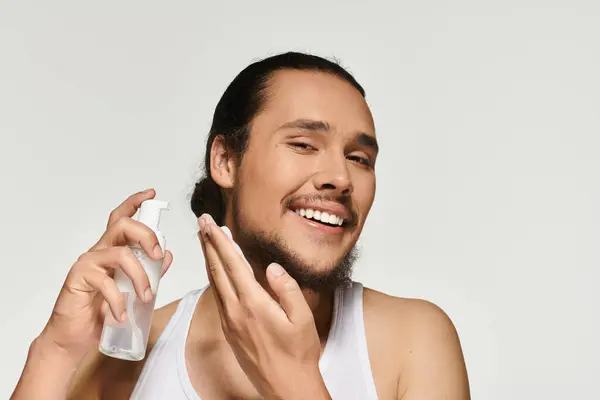Guapo joven barbudo disfruta aplicando cuidado de la piel mientras muestra un comportamiento alegre. — Stock Photo