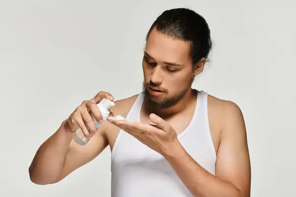 Young bearded man carefully dispenses grooming product into his palm in a well lit environment. — Stock Photo