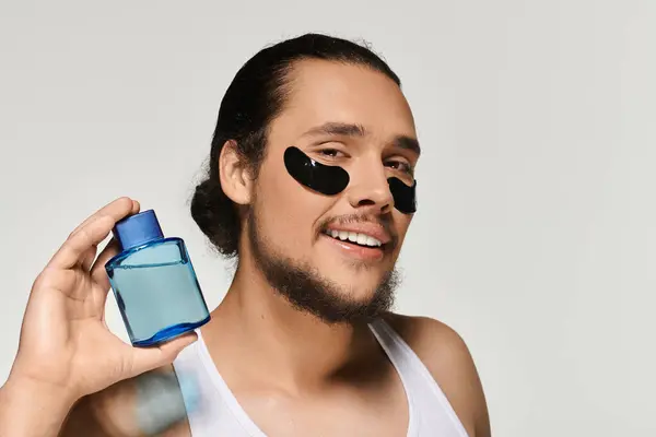 Young man with a beard displays facial treatment products while smiling widely, enjoying self care. — Stock Photo