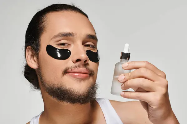 Young bearded man enjoys self care ritual with serum and eye patches for a fresh look. — Stock Photo
