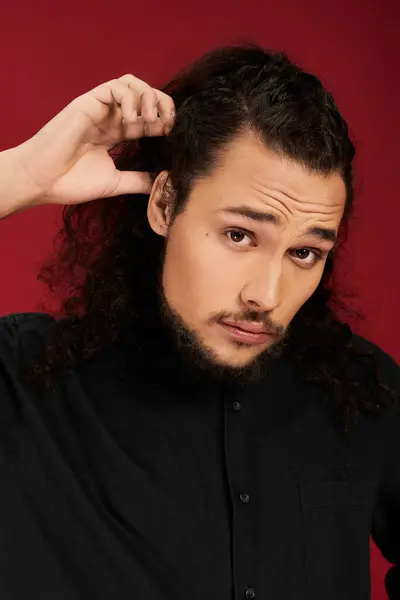 A handsome young man with a beard playfully adjusts his curly hair in striking light. — Stock Photo