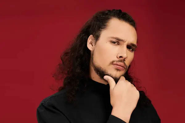 Young man with a striking beard poses thoughtfully, exuding charm against a deep red backdrop. — Stock Photo