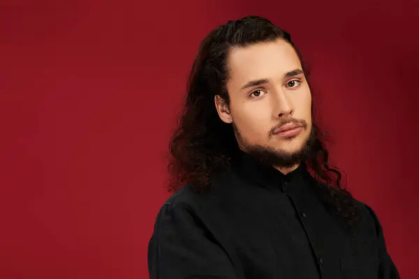 Charming young man with a beard stands proudly in front of a bold red background. — Stock Photo