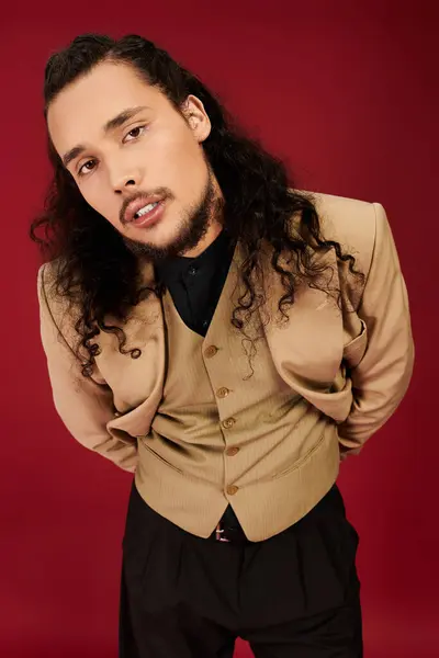 Handsome young man with a beard poses confidently in fashionable clothing on a bold red background. — Stock Photo