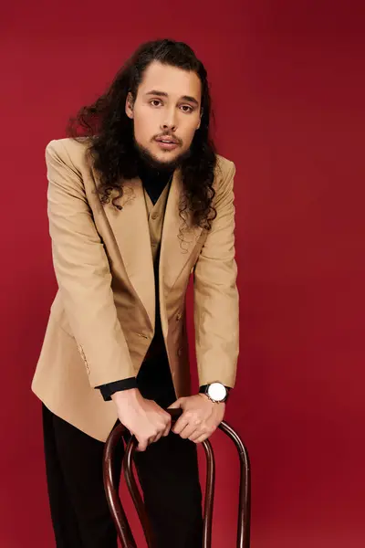 Confident young man with a stylish beard stands with a chair, exuding charm in a bold setting. — Stock Photo
