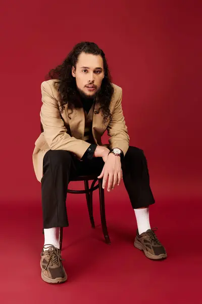 A handsome young man with a beard and curly hair poses on a chair, exuding style and charm. — стоковое фото
