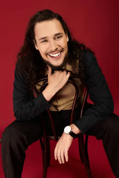 A handsome young man with curly hair and a beard smiles warmly while seated, emanating charm. — Stock Photo