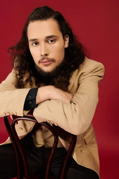 A bearded young man sits casually, exuding charm and style while leaning on a wooden chair. — Stock Photo