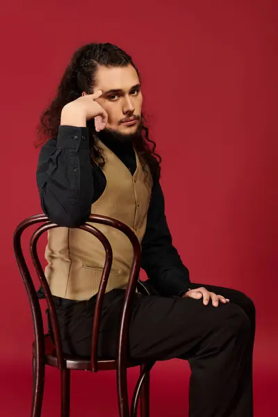 Young man with a beard exudes confidence while seated, lost in contemplation against bright red. — Stock Photo