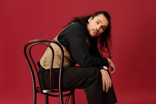 Handsome young man with a beard sits casually on a chair, showcasing his distinctive fashion sense. — Stock Photo
