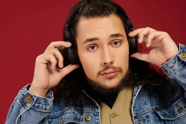 Young bearded man listens to music with headphones, showcasing his stylish denim jacket and focus. — Stock Photo