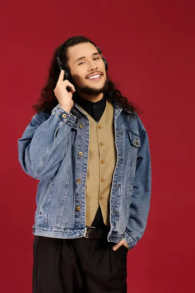 Bearded young man smiles and showcases a stylish outfit while listening to music. — Stock Photo