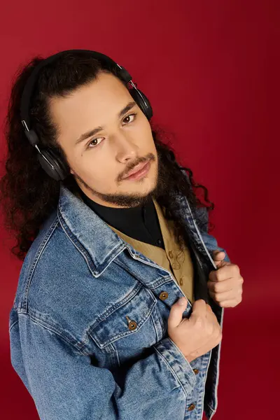 Bearded young man poses stylishly with music against a bold red background. — Stock Photo
