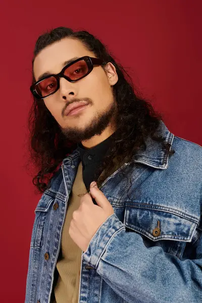 Handsome young man with a beard and stylish sunglasses confidently posing with a denim jacket. — Stock Photo