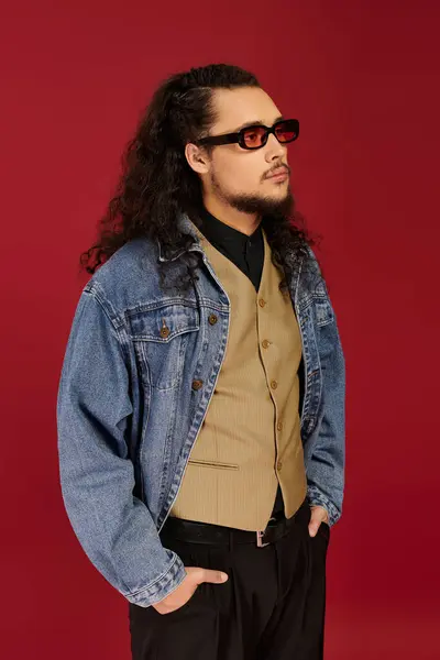 A bearded young man stands poised, wearing a chic outfit, immersed in a striking red environment. — Stock Photo