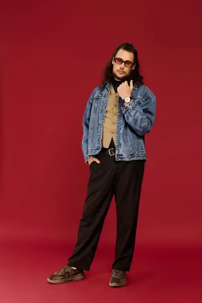 Young man with a beard showcases a stylish outfit and relaxed demeanor in a deep red setting. — Stock Photo