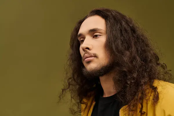 A young man with a thick beard and long, curly hair gazes thoughtfully with a serene expression. — Stock Photo
