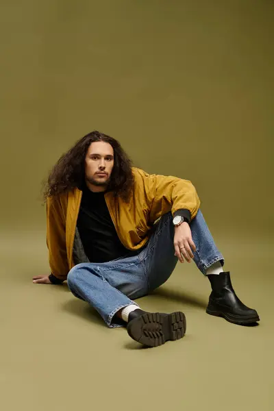 A stylish young man with a beard sits confidently on a neutral surface. — Stock Photo