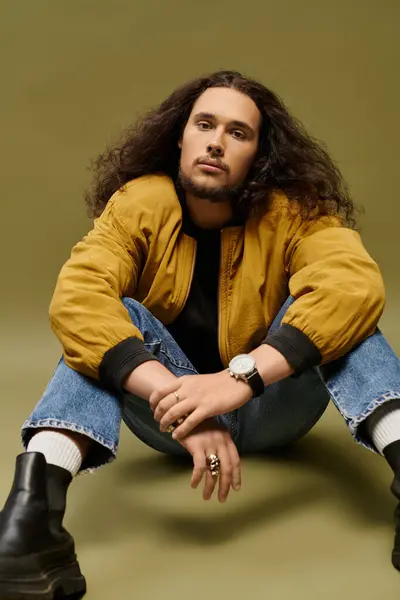 A young bearded individual exudes charm while seated casually against a vibrant green backdrop. — Stock Photo