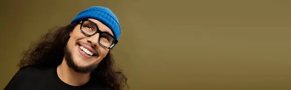 A handsome young man with a beard and glasses exudes charm while smiling, wearing a colorful beanie. — Stock Photo
