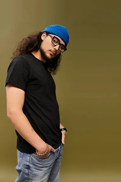A stylish young man with a beard and glasses wears a black shirt and blue beanie. — Stock Photo