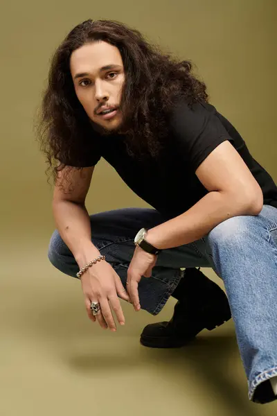 A confident young man with a beard crouches stylishly while showcasing his casual attire. — Stock Photo