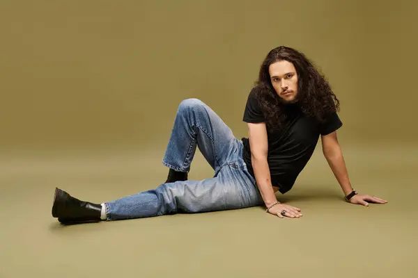 A stylish young man with a beard relaxes confidently against a soft green backdrop. — Stock Photo