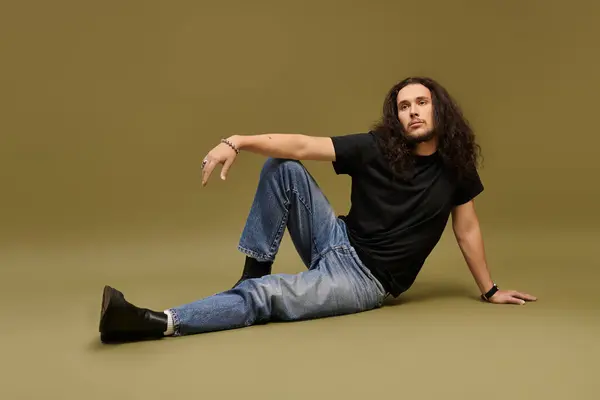 A young man in a black shirt and jeans poses confidently against a green background. — Stock Photo