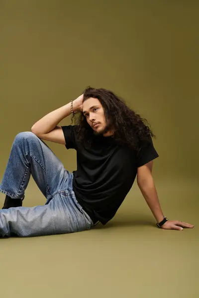 A handsome young man with a beard lounges against a minimalist green background, exuding confidence. — Stock Photo