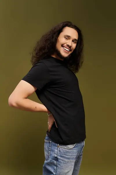 Smiling young man with a beard showing a playful pose, wearing a black shirt and jeans. — Stock Photo