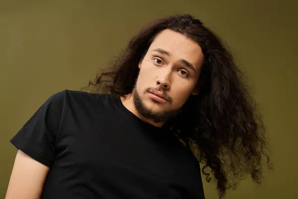 A young man with curly hair and a beard looks thoughtful in a casual outfit. — Stock Photo