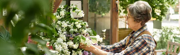 In a lush garden, a lovely senior woman carefully arranges a colorful bouquet of fresh flowers. — Stock Photo