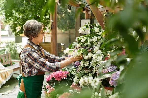 Beautiful senior woman lovingly arranges vibrant blooms in her peaceful garden sanctuary. — Stockfoto