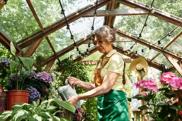 In a peaceful garden, a senior woman lovingly waters blooming flowers, embracing natures beauty. — Stock Photo