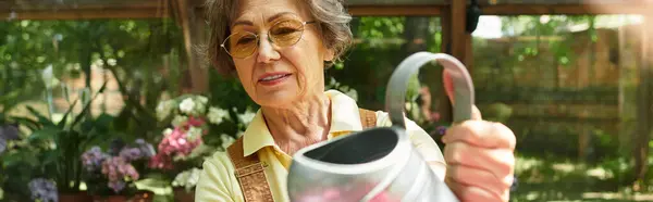 An elegant senior woman gathers joy in her garden as she waters blooming flowers under the sun. — Stock Photo
