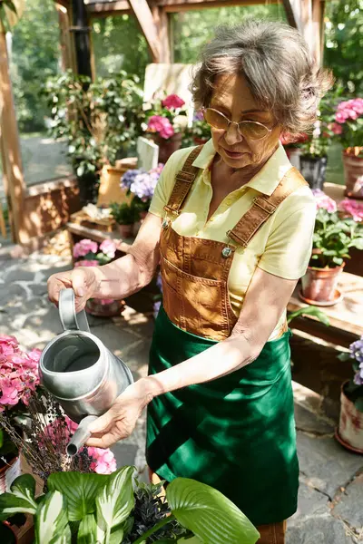 A senior woman happily waters her colorful flowers in a lush garden surrounded by nature. — Stock Photo