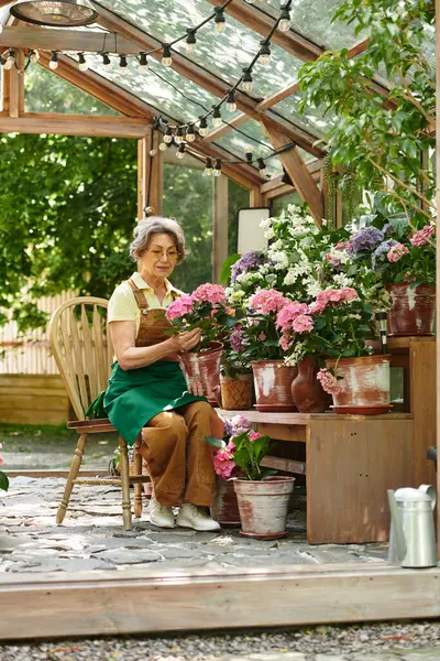 Elderly woman carefully arranges colorful flowers while enjoying a peaceful moment in her garden. — Stock Photo