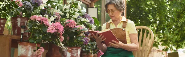 A senior woman relaxes while reading a book, surrounded by colorful flowers in a garden setting. — Stock Photo
