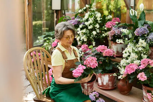 Senior woman tenderly cares for vibrant flowers in a charming garden setting filled with color. — стоковое фото