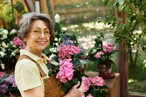 A beautiful senior woman smiles radiantly while tending to colorful flowers in a lush garden. — стокове фото