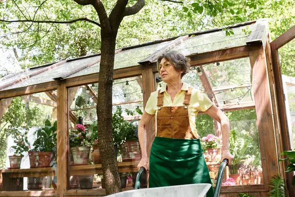 Joyful senior woman enjoys serenity in her garden, surrounded by blooming plants and trees. — Stock Photo