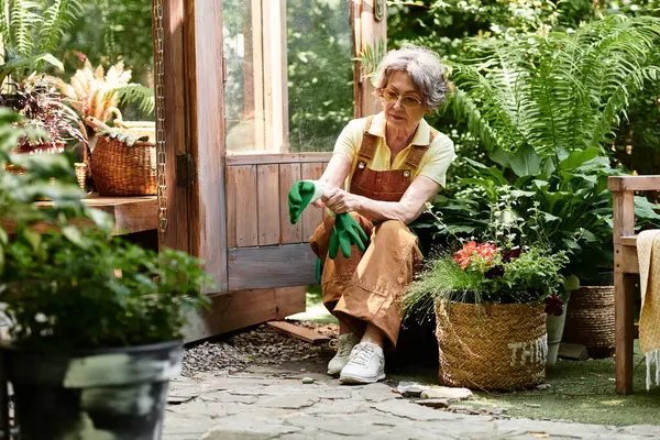 A senior woman prepares to tend her lush garden, surrounded by greenery and colorful flowers. — Stock Photo