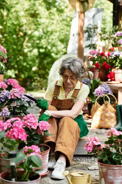 Beautiful senior woman carefully prunes flowers in a serene garden surrounded by greenery — стоковое фото